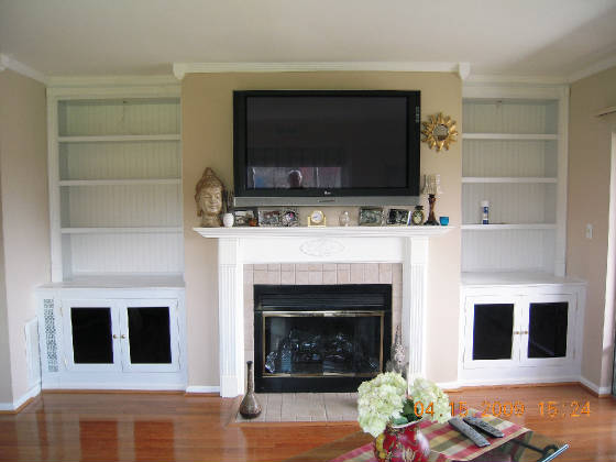 A TV set up above the fireplace with white wooden shelves on either side, creating a balanced and functional entertainment area